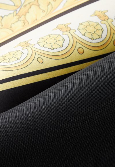 Tkanina se vzorem s zlatými květinovými motivy a černým strukturovaným materiálem, ukazující hladké a tkané textury v kontrastní barevné paletě.