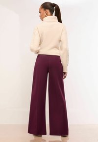 Pulover crem cu guler înalt și mâneci texturate, asociat cu pantaloni largi de un burgund închis. Material neted, croială lejeră, detalii minime.