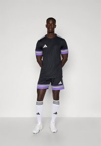 Černý atletický dres a šortky s fialovými a zelenými akcenty. Má tři bílé pruhy na ramenou a ponožky ve stejném stylu.