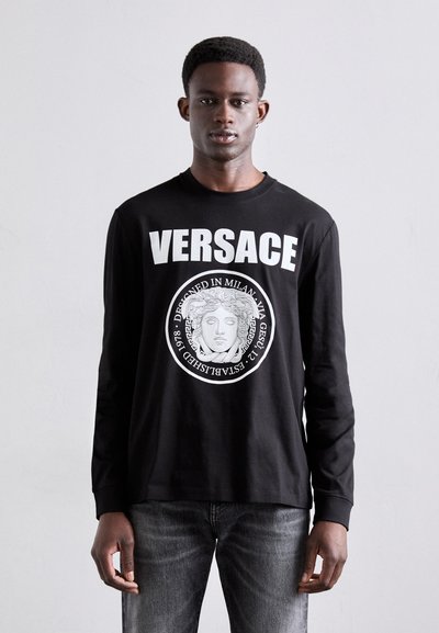 Schwarzes Langarm-T-Shirt aus Baumwolle mit weißem "VERSACE"-Text und einem kreisförmigen Grafikdesign mit einer klassischen Maskenmotivik. Slim Fit.