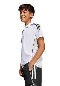 Polo bianco con colletto, maniche corte e strisce laterali nere. Tessuto con un aspetto texture, indossato con pantaloni sportivi neri abbinati.