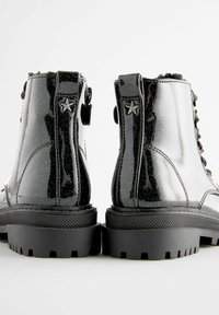 Bottines en cuir verni noir avec une finition brillante, présentant un détail en forme d'étoile et des semelles en caoutchouc noir texturé.