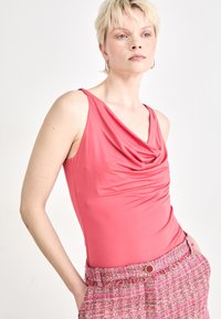 Fuchsia Body mit Cowl-Neck und glattem, dehnbarem Material, kombiniert mit einem pinkfarbenen Textrock mit Knopfdetail.