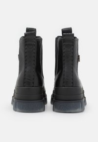Paire de bottines noires à plateforme avec languettes de tirage marquées et semelles épaisses foncées translucides, vues de dos sur fond blanc.