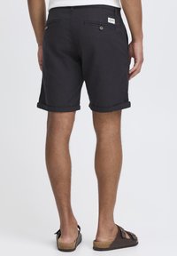 Pantalones cortos en gris oscuro hechos de una tela ligera, con puños doblados, bolsillos traseros con botones y una pequeña etiqueta de la marca en la cintura.