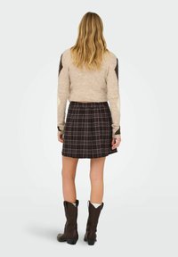 Suéter de lana beige con acentos marrones, combinado con una falda tableada de cuadros en negro. Botas vaqueras marrones con un tacón bajo completan el atuendo.