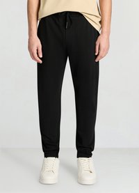 Black jogger pants made of soft fabric, featuring an elastic waistband with drawstring, side pockets, and tapered ankle cuffs.