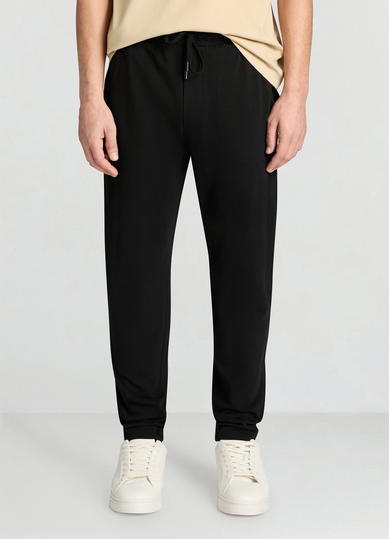 Black jogger pants made of soft fabric, featuring an elastic waistband with drawstring, side pockets, and tapered ankle cuffs.