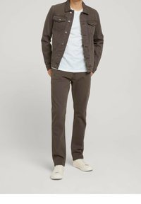 Veste en denim gris avec fermeture à boutons, associée à un t-shirt blanc et à un pantalon slim beige. Des baskets blanches complètent l'ensemble.