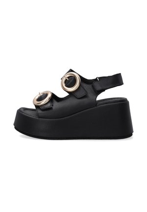 Black leather wedge sandal featuring large metallic circular accents, open toe design, and adjustable strap. Textured sole for grip.