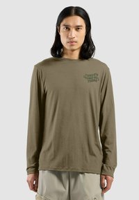 Langärmliges, olivgrünes Baumwoll-T-Shirt mit Rundhalsausschnitt und Frontdruck. Weiche Textur und lockere Passform, kombiniert mit beigen Shorts.