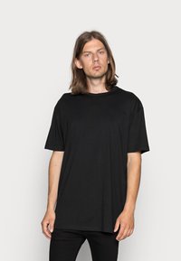 Camiseta negra de manga corta en un corte relajado, fabricada en suave tejido de algodón, con un clásico escote redondo y sin patrones ni adornos visibles.