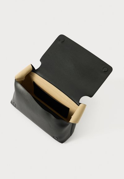 Crna kožna clutch torba s bež unutrašnjošću, koja sadrži zaobljeni preklop i kopču na gumb. Unutra se nalazi crna torbica za organizaciju.