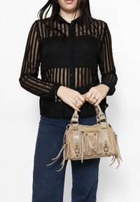 Camicia nera trasparente con bottoni e strisce verticali, abbinata a una borsa a tracolla color beige chiaro con dettagli in metallo e frange.