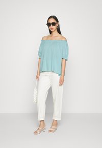 Blusa azul clara sem mangas com mangas curtas e volumosas, combinada com calças brancas de corte relaxado e sandálias brancas de tiras.