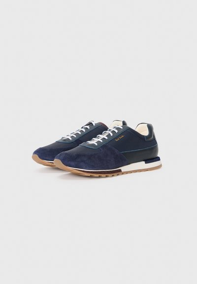Navy sneakers with a mix of suede and leather, featuring white laces, a tan rubber sole, and gold detailing on the side.