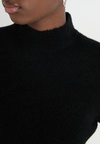 Pulover negru, cu guler înalt și model nervurat, care se potrivește perfect pe corp. Textură moale, care evidențiază fibrele fine, cu un design minimalist și fără cusături.