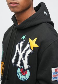 Czarna bluza z kapturem z dużym białym haftowanym logo "NY", kolorowymi naszywkami z gwiazdą, różą i tekstowymi akcentami na klatce piersiowej i rękawie.