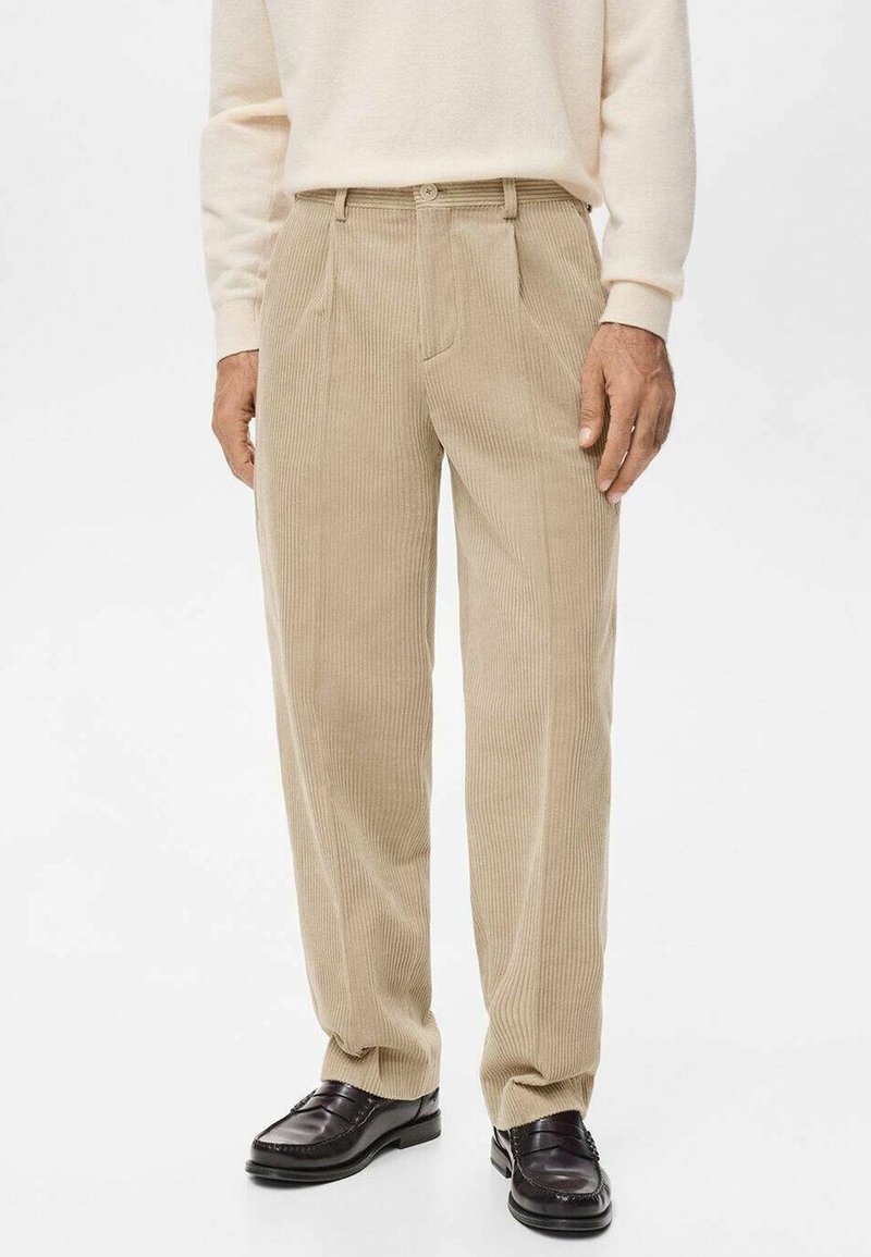 Pantalones de pana beige con un corte recto, que presentan pliegues definidos, bolsillos laterales y una cinturilla lisa. Combinados con mocasines negros.