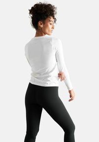 Langærmet hvid atletisk top med en glat tekstur, featuring rund halsudskæring og tætsiddende design, parret med sorte tights.