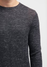 Pull en maille gris foncé avec un motif texturé, col rond et manches longues. Le matériau semble doux avec un effet subtil moucheté.