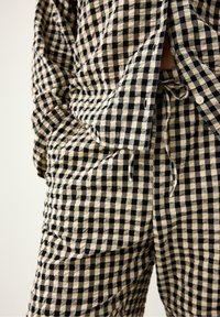 Czarny i kremowy komplecik piżamowy w kratkę, składający się z zapinanego na guziki topu z kieszeniami i spodni z paskiem ściągającym, wykonany z lekkiego materiału.