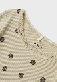 Geribbelde beige top met bruine bloemenpatronen, voorzien van kantafwerking rond de halslijn en een kleine strikdetail bij de kraag.