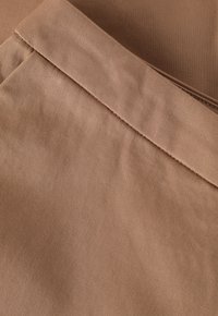 Tissu marron avec une texture lisse et un éclat subtil. Les détails de couture sont visibles près de la taille et le long des bords.