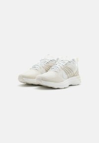 Scarpe da corsa leggere in mesh bianco e beige con dettagli testurizzati, lacci piatti e una suola spessa e ammortizzata.
