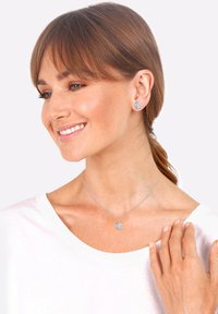 Silberne Schneeflockenohrringe und passendes Halsband, mit einer zarten Kette und einem aufwendigen Schneeflockenanhänger-Design. Über einem weißen Oberteil getragen.