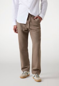 Beige, löst sitzende Hose aus weichem Stoff, mit elastischem Bund und Kordelzug, kombiniert mit hellen Sneakern.