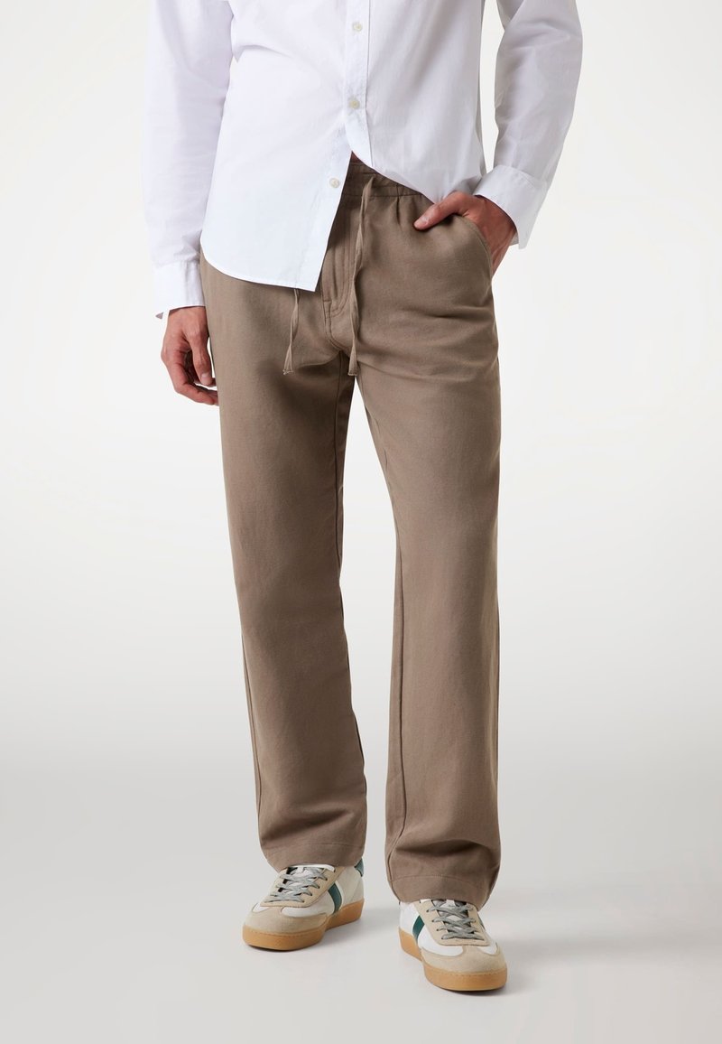 Beige, löst sitzende Hose aus weichem Stoff, mit elastischem Bund und Kordelzug, kombiniert mit hellen Sneakern.