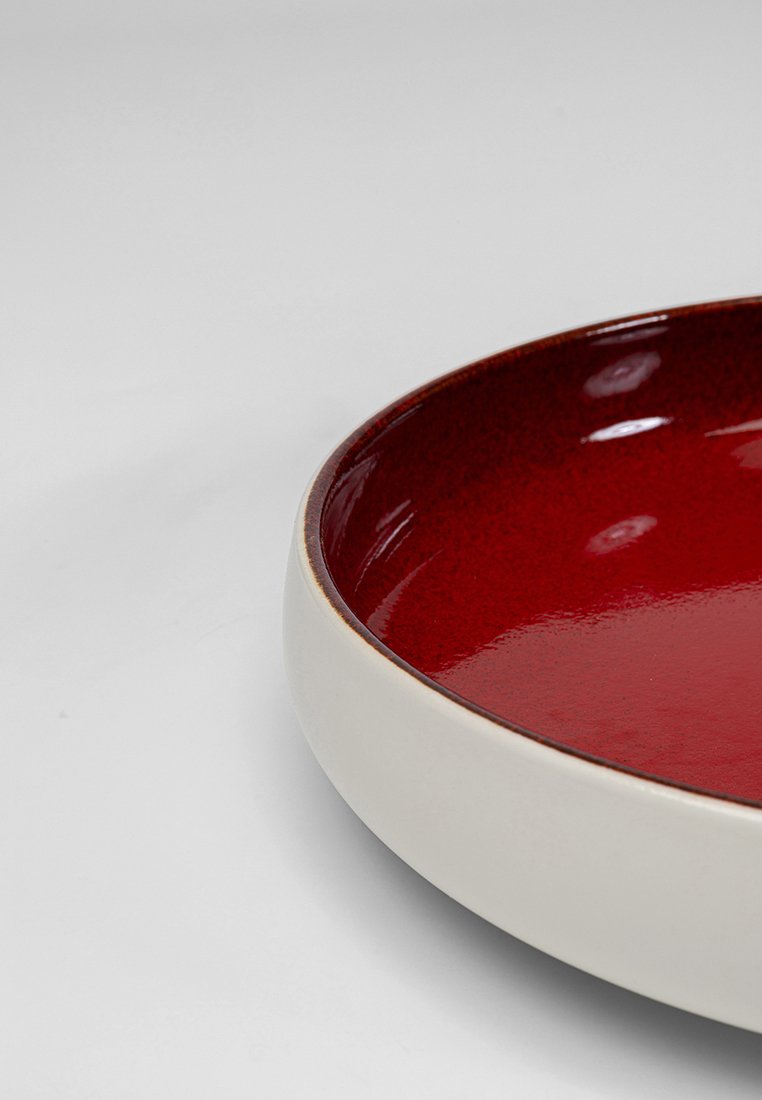 Keramische Schüssel mit einem tiefroten, glänzenden Innenraum und einer glatten weißen Außenseite, mit einem leicht geschwungenen Rand und einem eleganten Design.