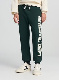 Ciemnozielone spodnie dresowe z białym napisem „ATHLETIC DEPT” wzdłuż lewej nogawki, wyposażone w elastyczny pas i regulowany sznurek.