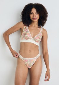 Kanten versierde, met bloemen geborduurde bralette en bijpassende string in zachte beige en roze tinten. Doorzichtige stof met decoratieve details.