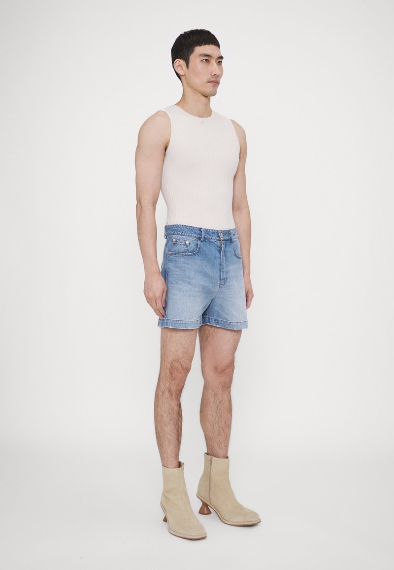 Débardeur beige à côtes légères, short en denim bleu avec poches avant, et bottines beige à talon. Texture lisse, coupe décontractée.