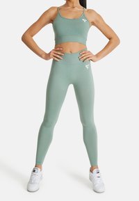 Jasnozielony sportowy biustonosz i legginsy z wysokim stanem wykonane z elastycznej tkaniny, z białym logo po lewej stronie i stylowym, dopasowanym krojem.