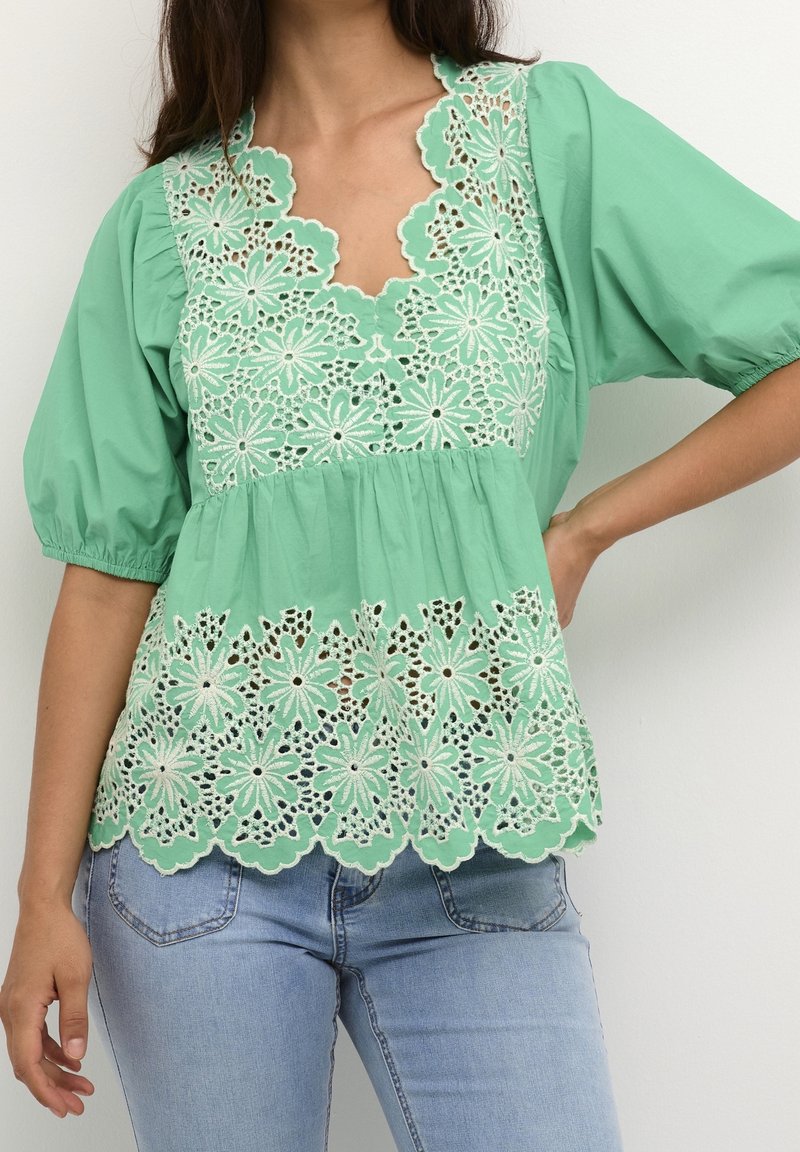 Haut vert menthe avec un bord en dentelle florale, manches courtes bouffantes et encolure en V. Tissu doux avec des détails en dentelle complexe le long de l'ourlet.