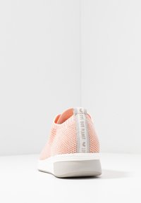 Světle růžová síťovaná teniska s texturovaným povrchem, bílou gumovou podešví a šedým poutkem s jemným nápisem "Milujeme naši planetu".