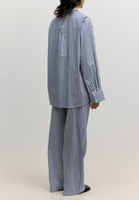 Gestreiftes Baumwoll-Pyjama-Set mit weit geschnittenen Hosen und einem langärmeligen Hemd mit Knöpfen in Blau und Weiß. Glatte Textur, lockere Passform.