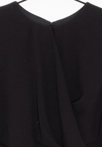 Mustapuku, jossa on laskostettu muotoilu takana, vetoketjukiinnitys kaulassa ja pehmeä, teksturoitu kangas. Minimalistinen tyyli, jossa on siistejä linjoja.