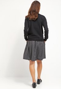 Czarny sweter z długimi rękawami, uzupełniony szarym plisowanym spódnicą, noszony z czarnymi butami. Gładki materiał i casualowy design.