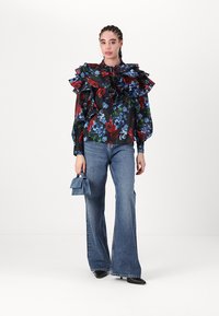 Black floral blouse with ruffled collar, featuring red and blue flowers. Paired with light blue flared jeans and a small blue handbag.