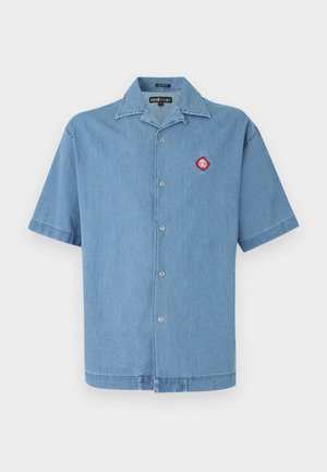 Chemise en jean bleu clair à manches courtes, boutonnée, col ouvert et petite écusson rouge en forme de losange sur la poitrine gauche.