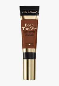Tube en bronze de fond de teint mat au fini doux et contrôle de l'huile Born This Way de Too Faced. Présente des accents dorés, un capuchon noir et est marqué "Tenue 24 heures" avec de l'acide hyaluronique.