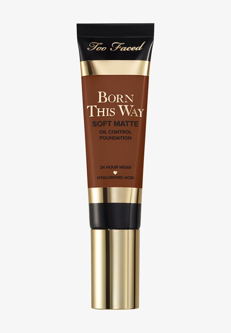 Tube en bronze de fond de teint mat au fini doux et contrôle de l'huile Born This Way de Too Faced. Présente des accents dorés, un capuchon noir et est marqué "Tenue 24 heures" avec de l'acide hyaluronique.