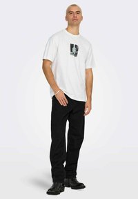 Maglietta bianca in cotone con stampa grafica sul petto, abbinata a pantaloni in velluto nero e stivaletti neri alla caviglia. Design semplice e casual.
