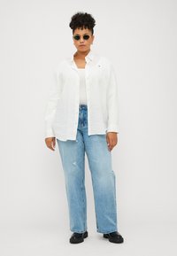 White linen button-up shirt over a white tank top, paired with light blue high-waisted jeans, and black chunky boots. Green sunglasses worn.