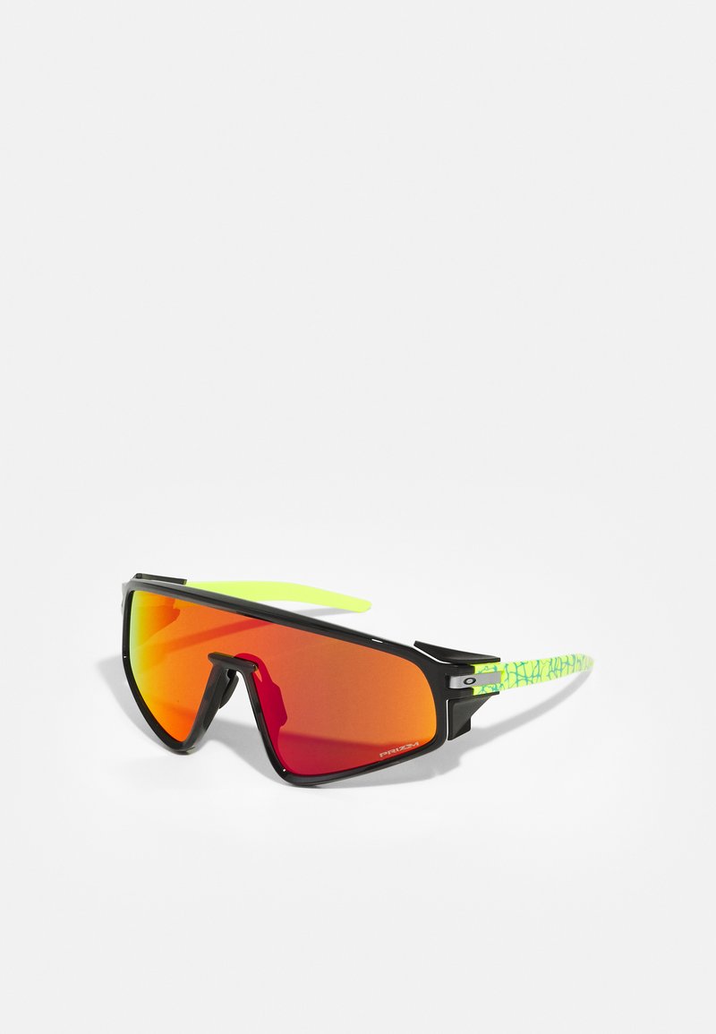 Óculos de sol desportivos com armação preta, lentes laranja de tamanho exagerado e hastes com padrão verde distinto. Design leve para uso ao ar livre.