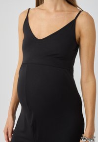 Black maternity dress with a V-neck and thin straps, made of soft, stretchy fabric. It features a fitted bodice and flared lower section.